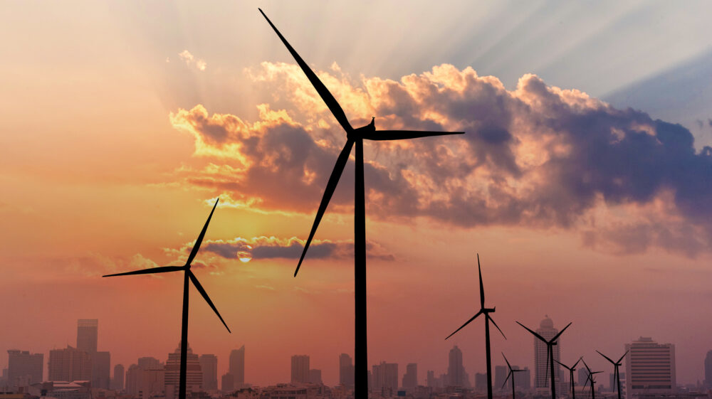 Silhouettes of wind turbines foreground a city skyline at sunset