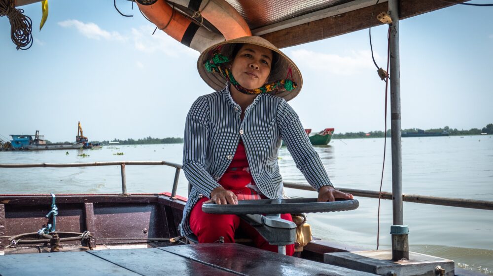 Woman wearing straw hat driving wooden boat, Mekong Delta, Viet Nam