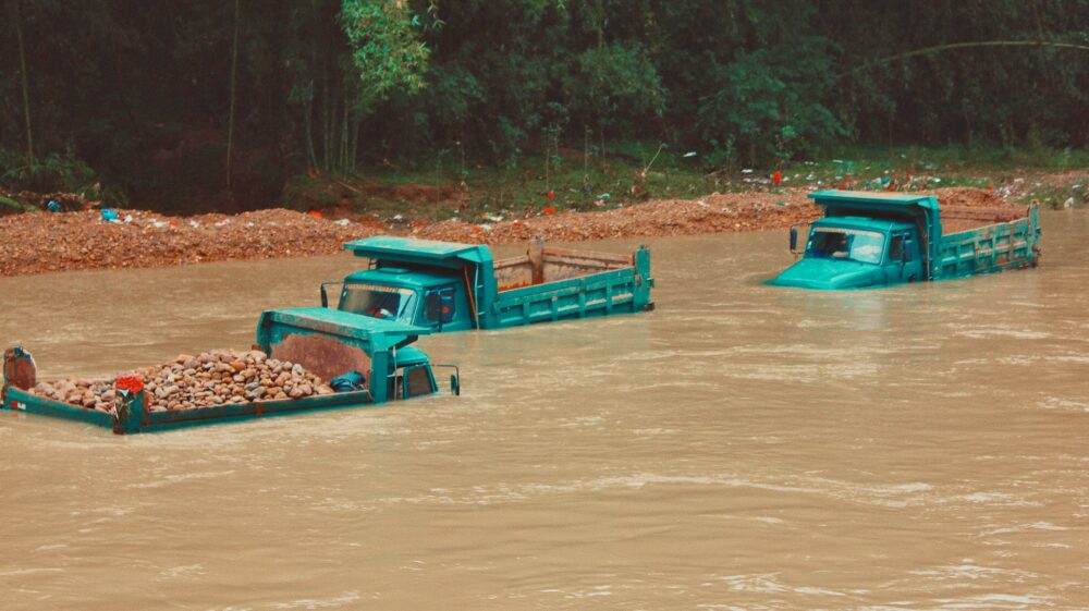 Green trucks submerged in muddy water