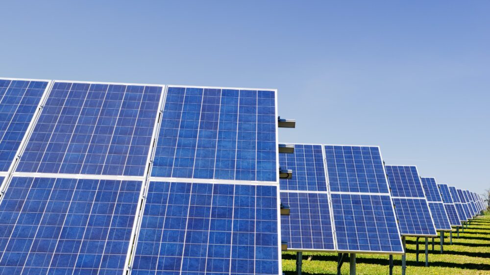A series of solar panels are tilted upward beneath a blue sky