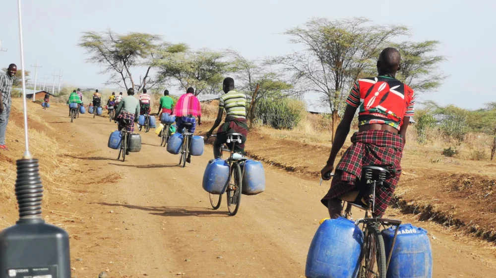 A group of people riding bikes down a road with carrying containers for water