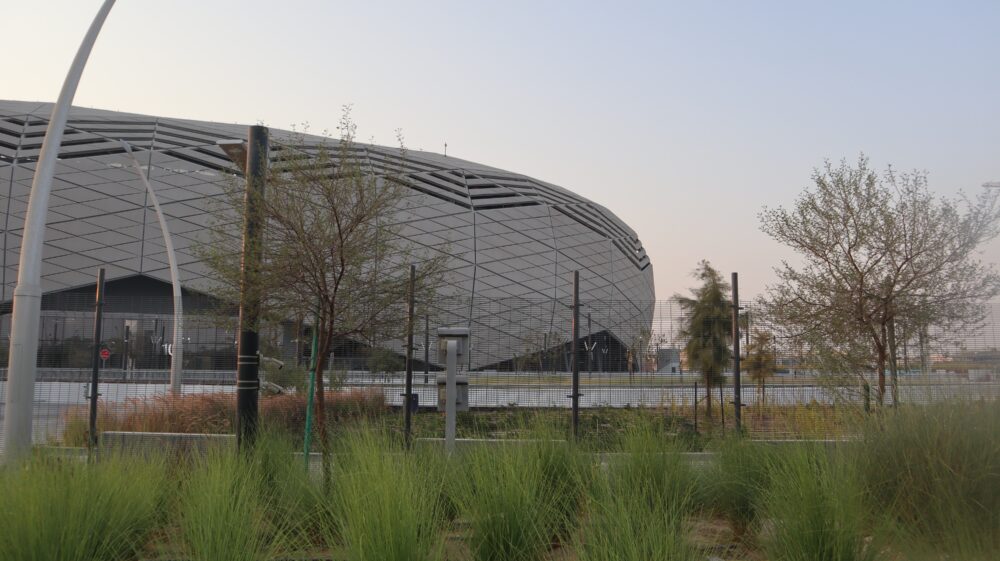 Education City stadium, a football stadium built for the 2022 World Cup, sits beneath a twilight sky, foregrounded by a landscape of grassy bushes