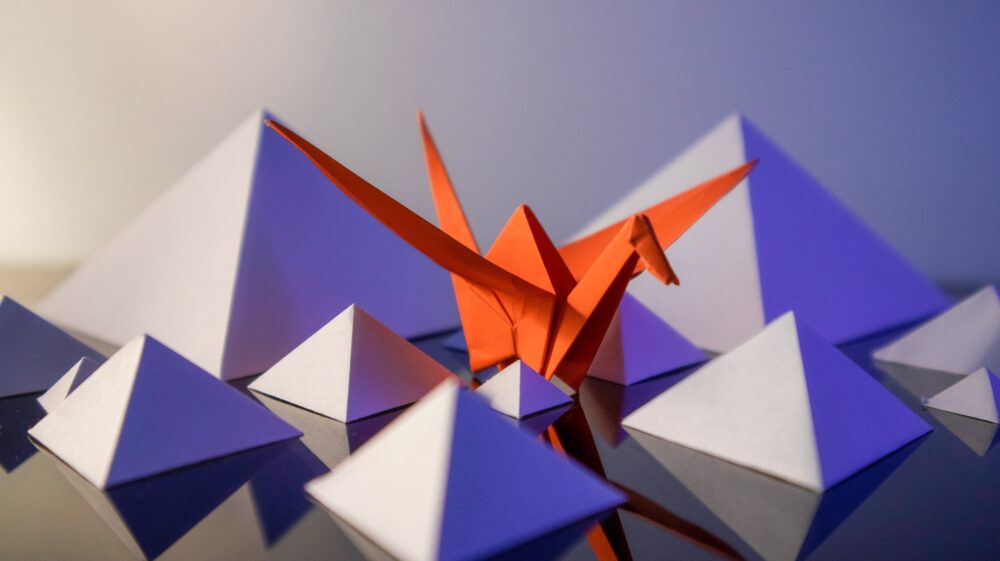 White paper pyramids with orange paper crane
