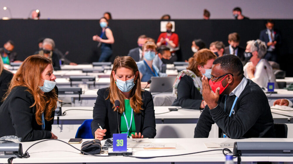 Three people in masks at a table in a meeting hall with others at COP26 attendees Glasgow