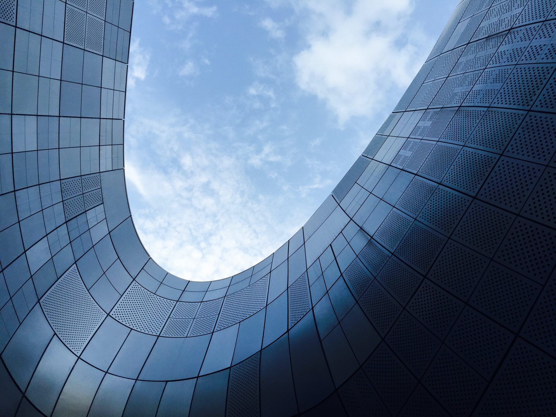 View from below of winding steel building under blue sky with clouds, Dongdaemun, Seoul, South Korea