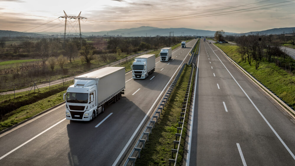 A convoy (or platoon) of white freight trucks on a highway