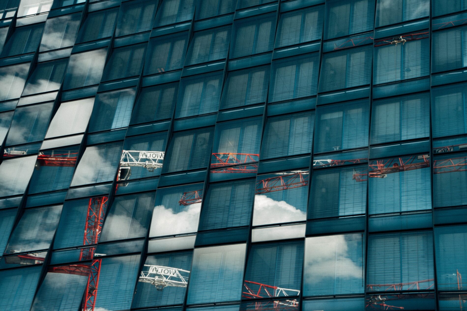 Construction cranes, clouds and blue sky are reflected against the glass sides of a new building