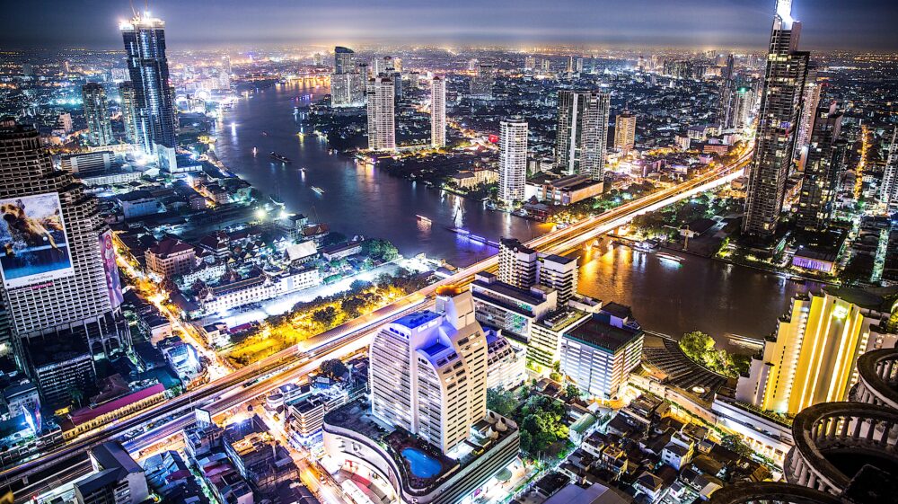 Aerial view of the Bangkok, Thailand nighttime skyline, bisected by the Chao Phraya River