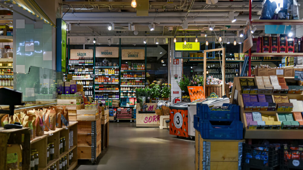 Urban Deli interior in Stockholm, showing grocery aisles, wooden crates of goods, and a yellow ‘Bröd’ (bread) sign overhead.