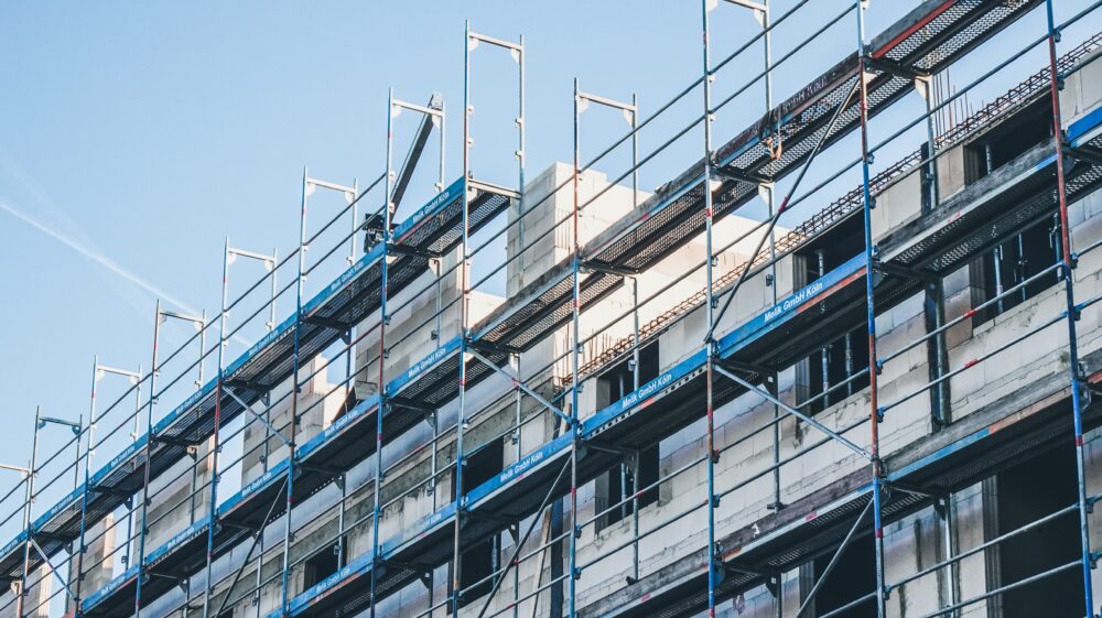Scaffolding covers an older building in Cologne, Germany, beneath a pale blue sky.