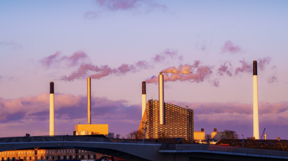 Power plant in Denmark emits pollutants against a pink and blue twilight sky.
