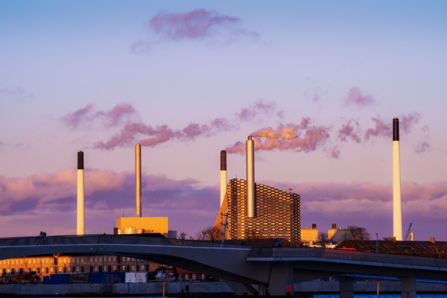 Power plant in Denmark emits pollutants against a pink and blue twilight sky.