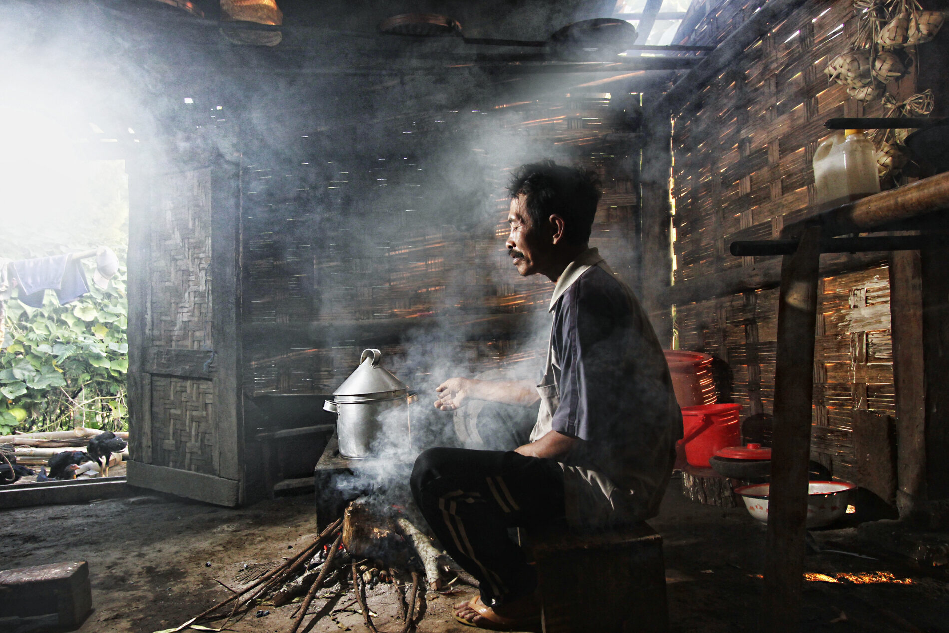 Side view of man sitting next to wood-burning stove in hut