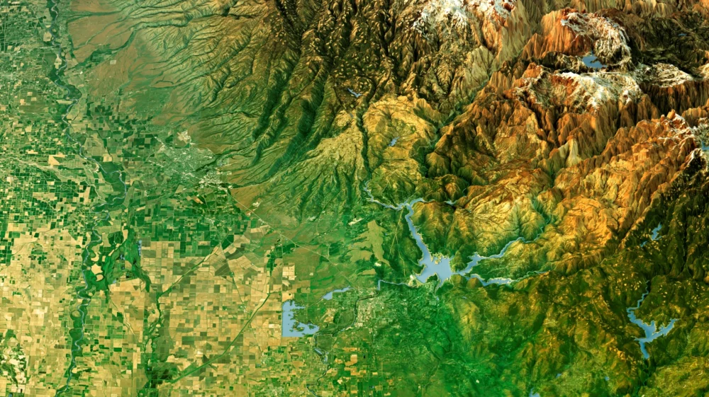 3D Render of a Topographic Map 3D View of Butte County, California. It shows lowlands dotted with agricultural fields to the bottom left giving way to tall, ragged mountains in the upper right corner, with some freshwater bodies scattered throughout.