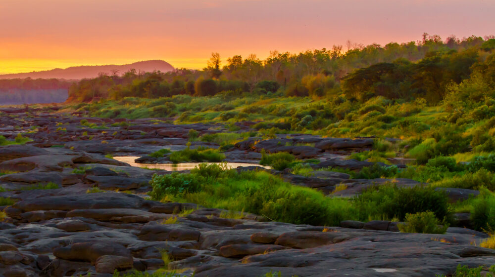 Sun rises over rocky banks of the Mekong River between Thailand and Lao PDR.