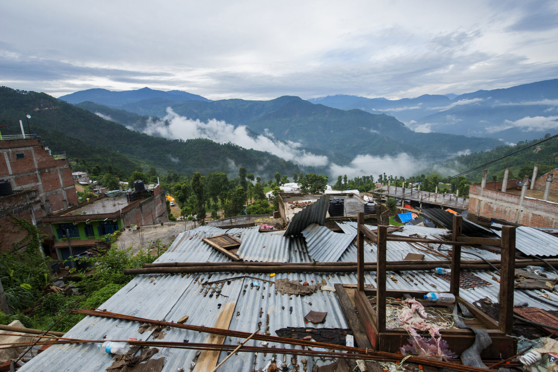 Buildings rattled by an earthquake in Nepal lie in ruins amid a summer monsoon, against a backdrop of lush forested mountains.