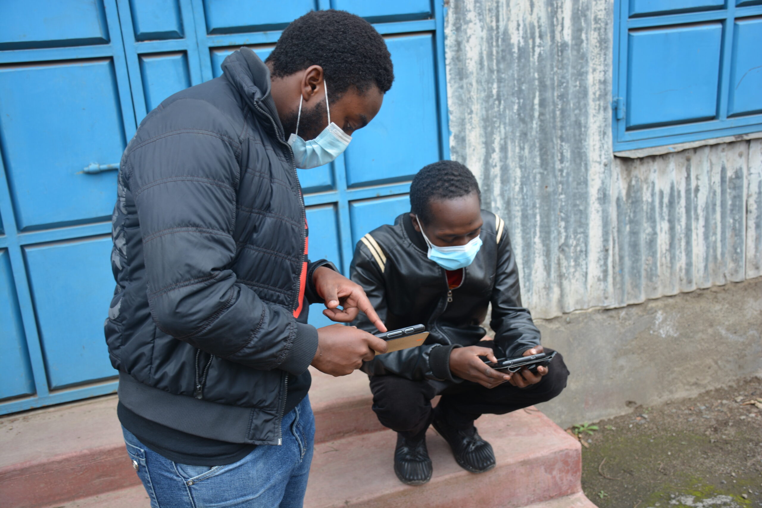 Two men wearing surgical masks looking on their phones.