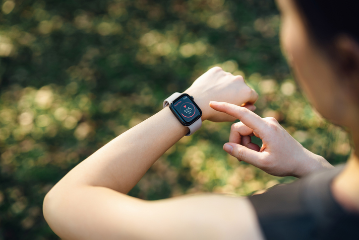 Over the shoulder view of a women in a green park, measuring the heart rate on her smartwatch.