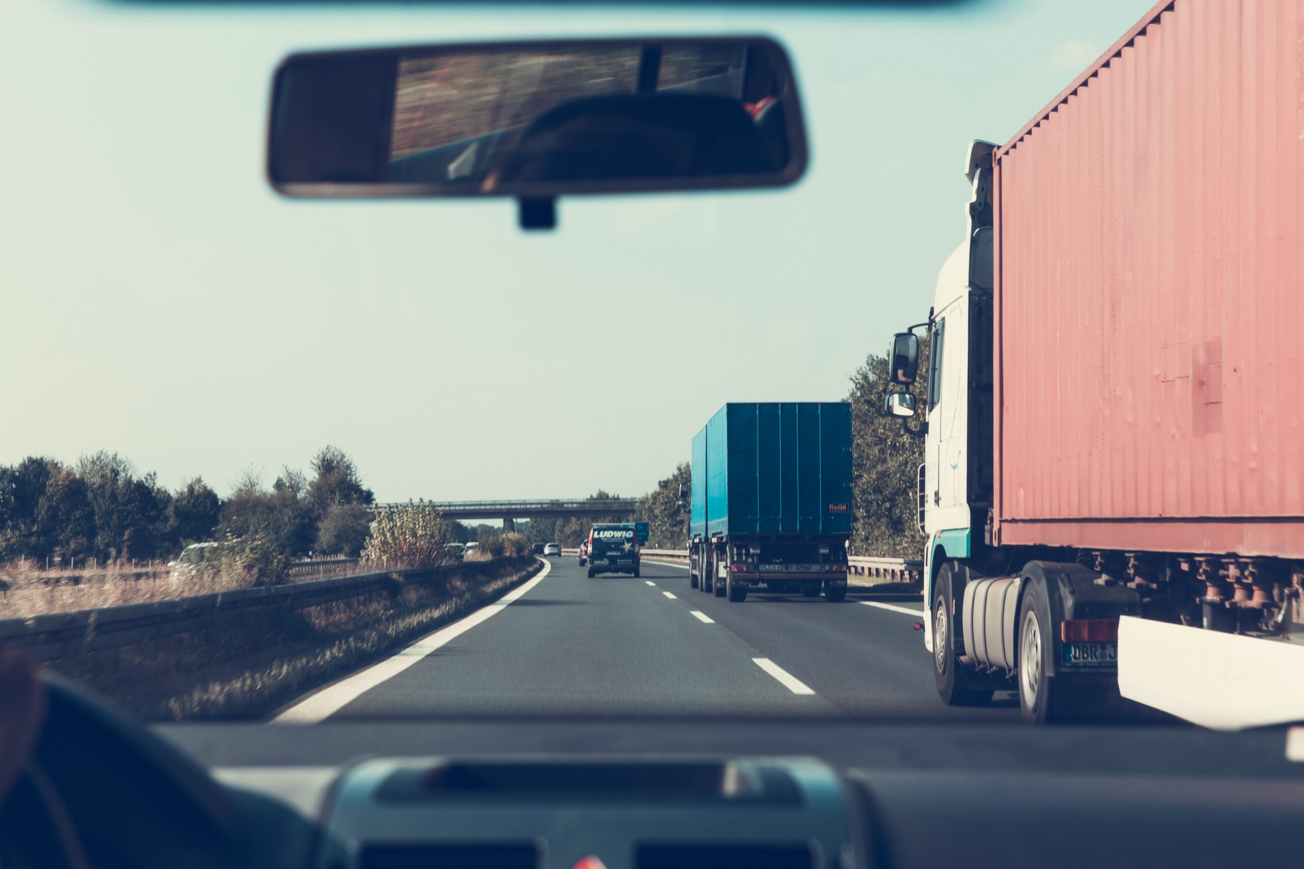 view from the front window of a car of a one-way two-lane road with a blue and a red truck driving past in the lane to the right