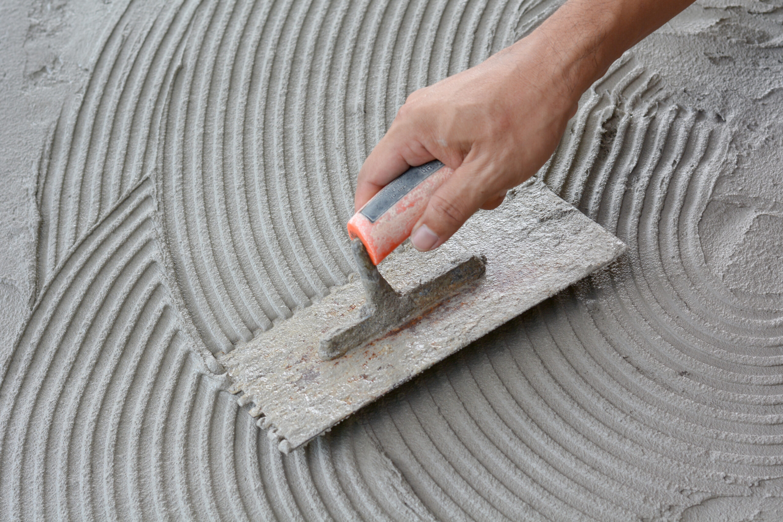 Hand on a spreading tool applying cement over a surface