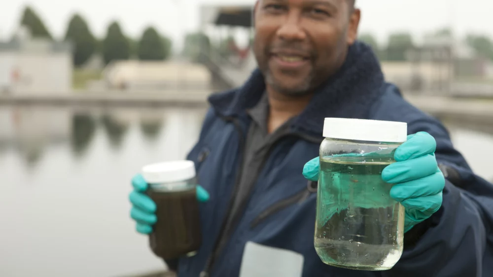 Man working at sewage treatment plant, holding water sample in hands.