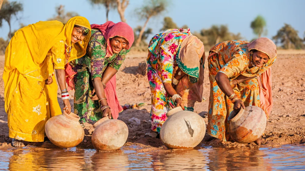 Indian women collecting water from the lake. Collecting and carrying water are women's responsibilities in India. Rajasthani women often walk long distances through the desert to bring back jugs of water that they carry on their heads. Thar Desert, Rajasthan. India.