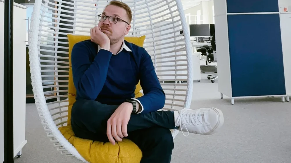 Ivo Krustok sitting in a basket swing chair in an office. He is leaning on leg over the other's knee and resting his head on his right hand.