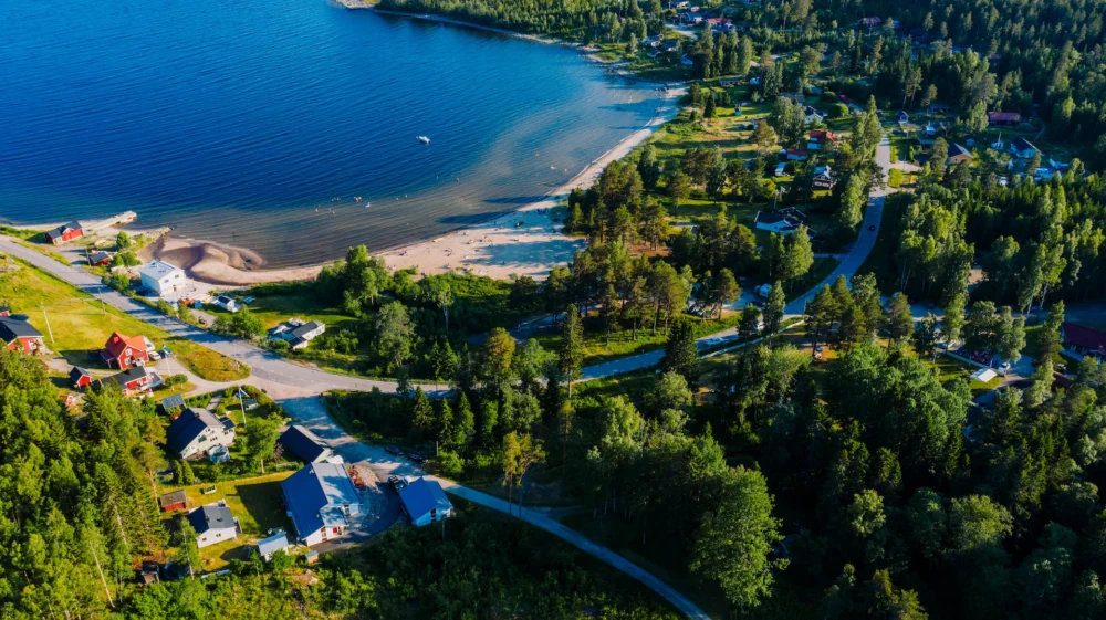 Aerial view of green trees and body of water during daytime. A small beach on the island of Alnö in Norrland, Sweden
