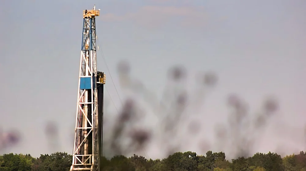 Fracking rig against a pale blue sky with trees in the background