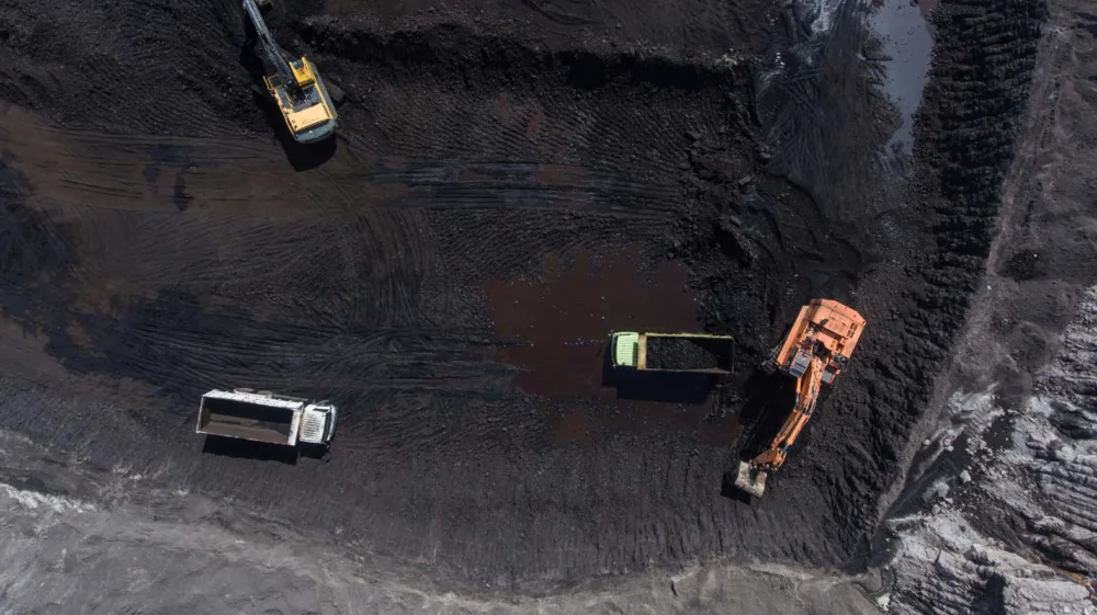 An aerial view of an open-pit mine in Indonesia with four large trucks.