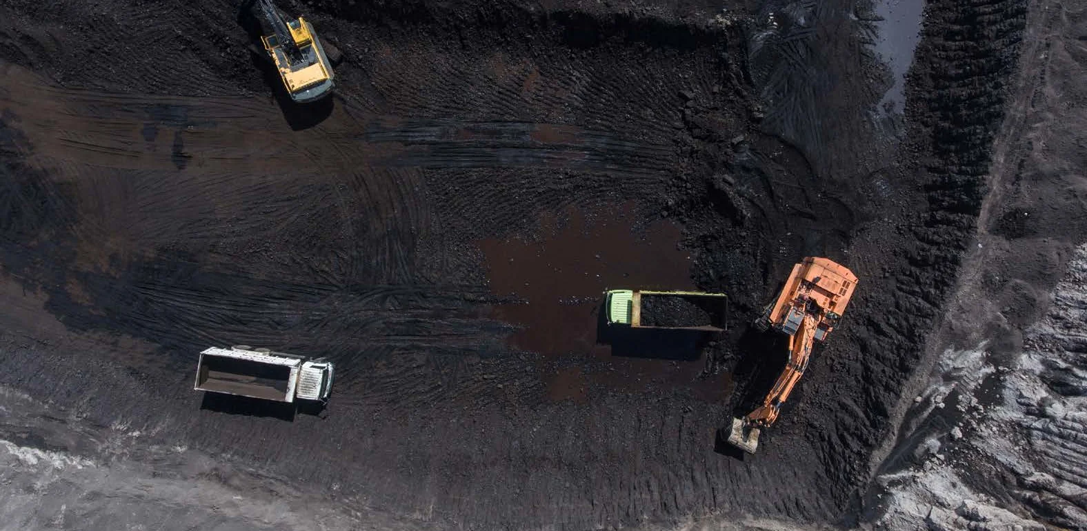 An aerial view of an open-pit mine in Indonesia with four large trucks.