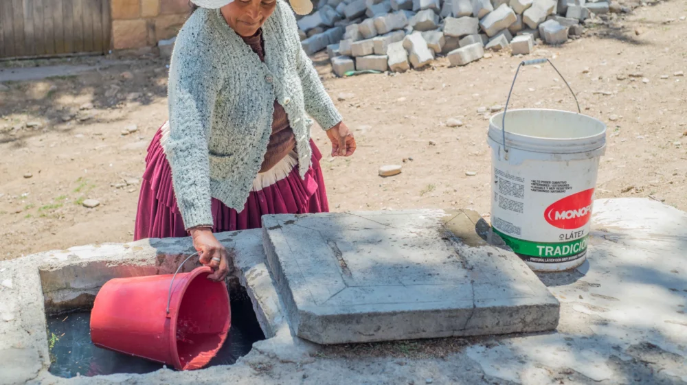 Woman collecting water from a rural reservoir tank, Taucachi community, La Paz, Bolivia