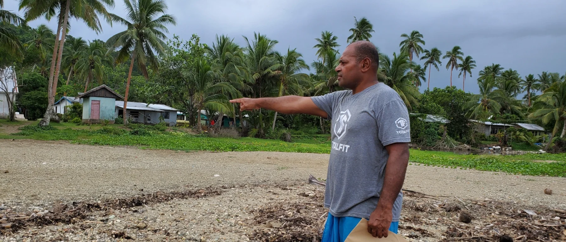 Man standing on a beach in Fiji, one arm extended and finger pointing, with paper in the hand by his side.