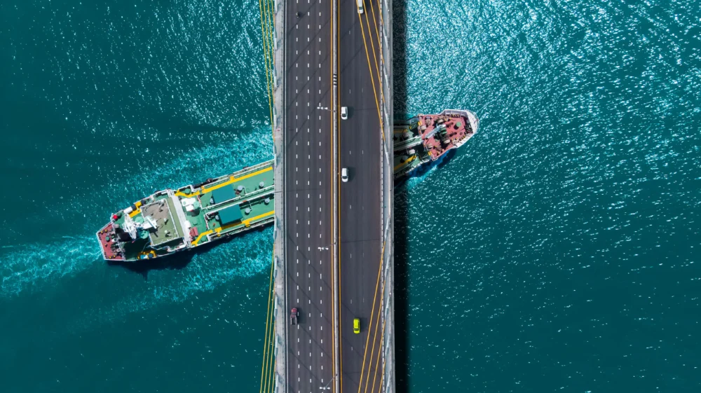 Aerial view over a turquoise sea where an oil tanker passes beneath a sling bridge.