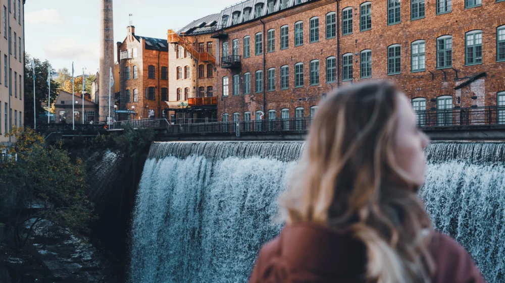 Blonde girl stands in front of a large waterfall, Motala Ström river.