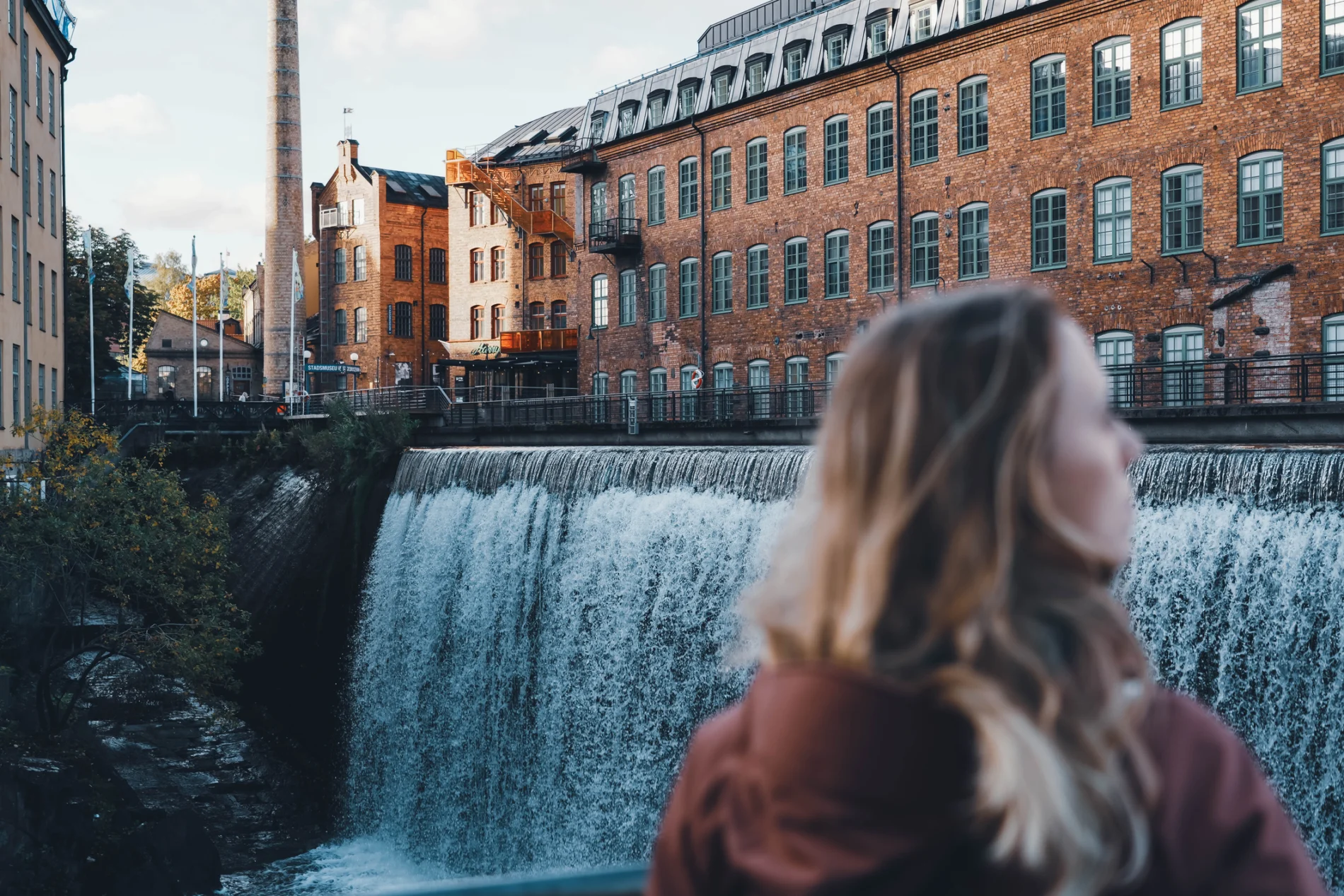 Blonde girl stands in front of a large waterfall, Motala Ström river.