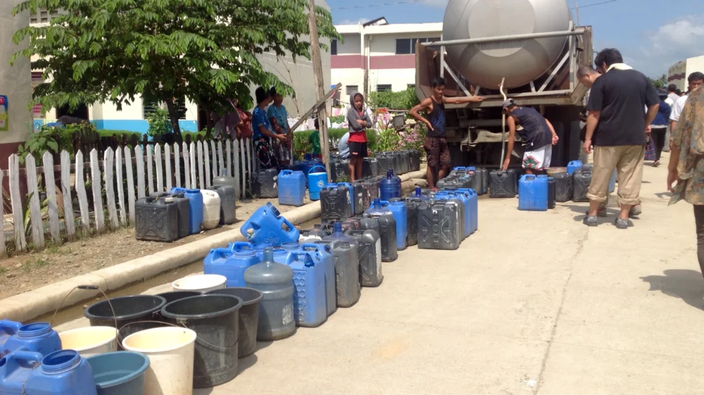 A line of blue, white and gray water containers snakes up to a silver water tanker.