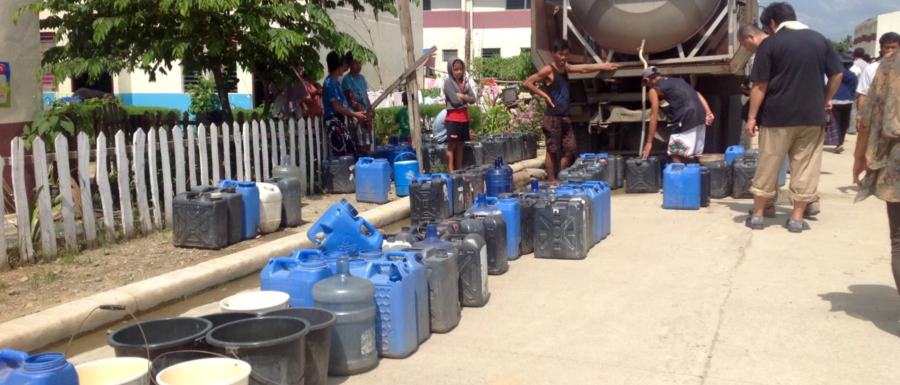 A line of blue, white and gray water containers snakes up to a silver water tanker.