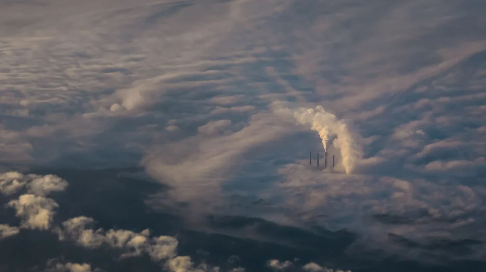 Aerial view of a sea of clouds punctuated with smoke stacks emitting pollution.