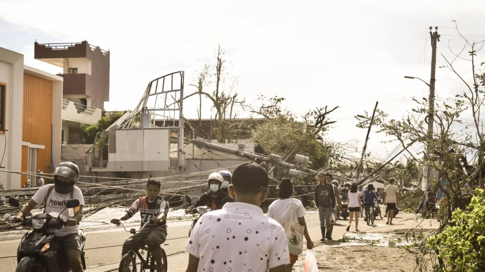 Residents navigate the damage wrought by Super Typhoon Odette in the Philippines, with trees and power poles toppled over smashed buildings.