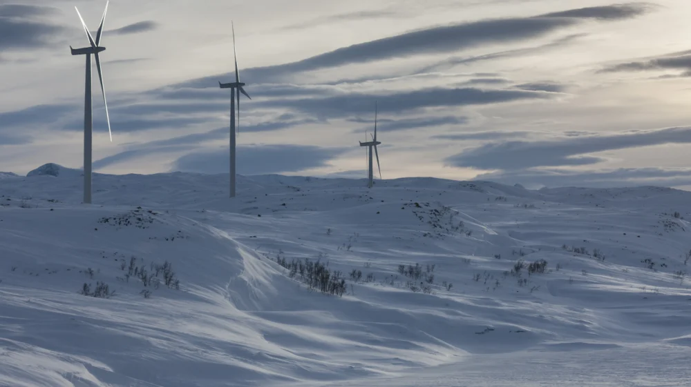 A small windfarm near Bjornafell, Sweden: three turbines atop a snow-covered hill and plain below under cloudy skies.
