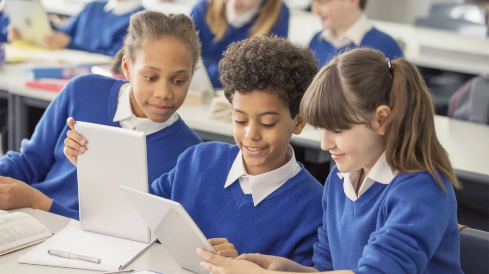 Three school children in a classroom looking at digital tablets
