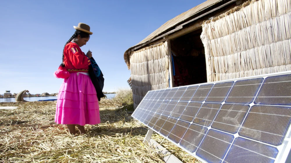 A Peruvian Indigenous woman on the Uros Islands of Lake Titicaca stands next to a solar panel.