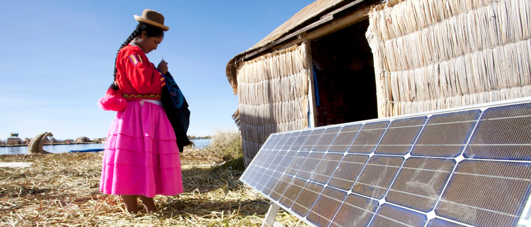 A Peruvian Indigenous woman on the Uros Islands of Lake Titicaca stands next to a solar panel.