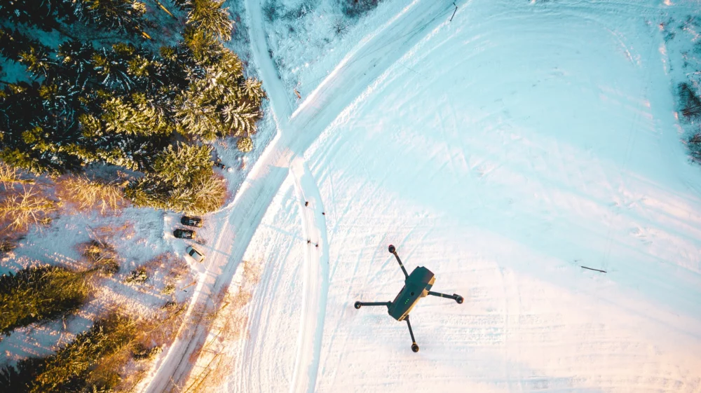 black quadcopter drone flying over snow field during daytime