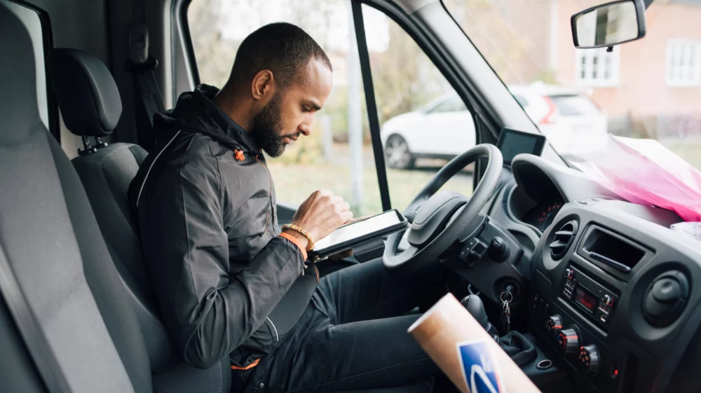 Side view of male worker using digital tablet while sitting in delivery van