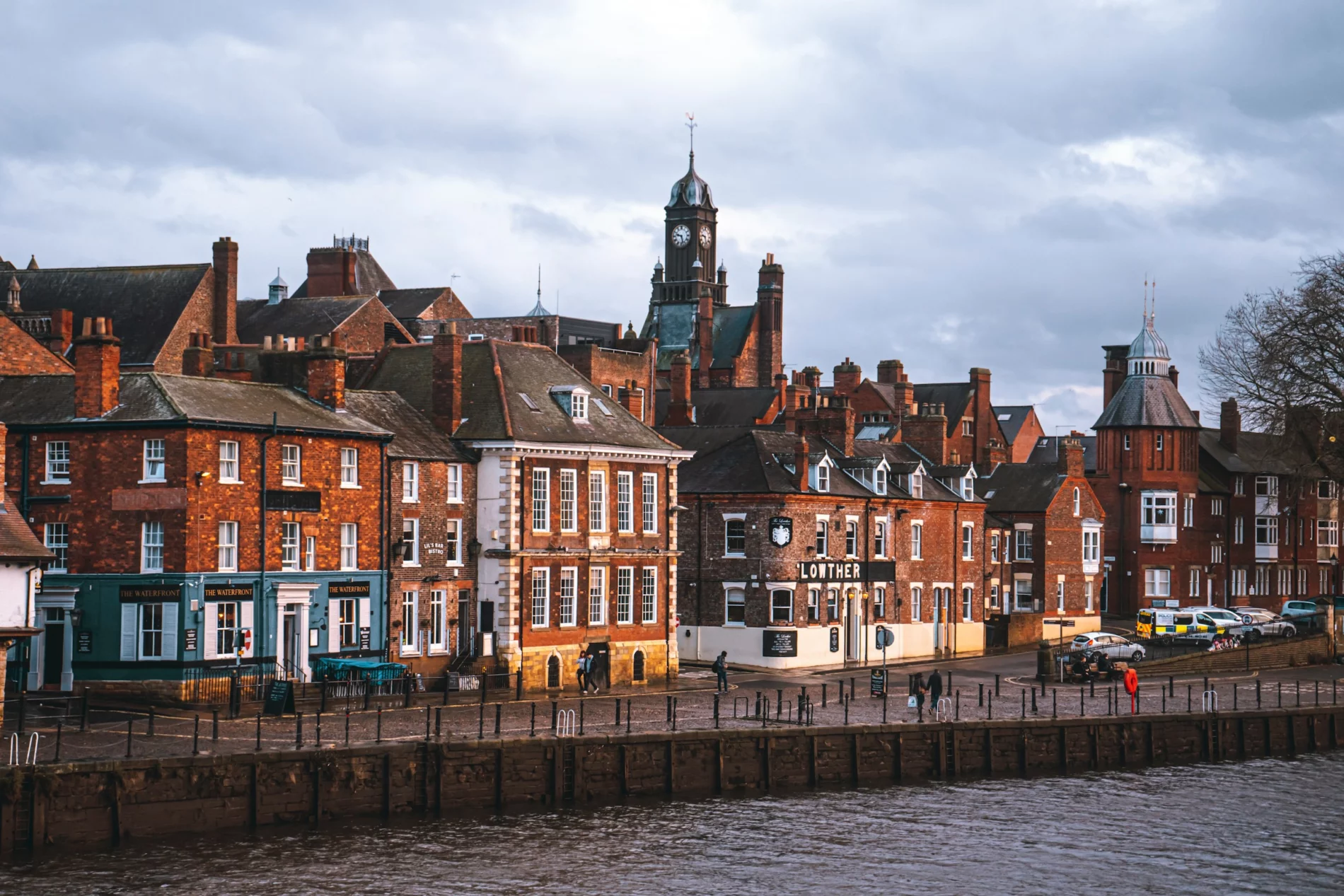 Brick buildings on the along a bollarded road on the edge of the river Ouse in York.