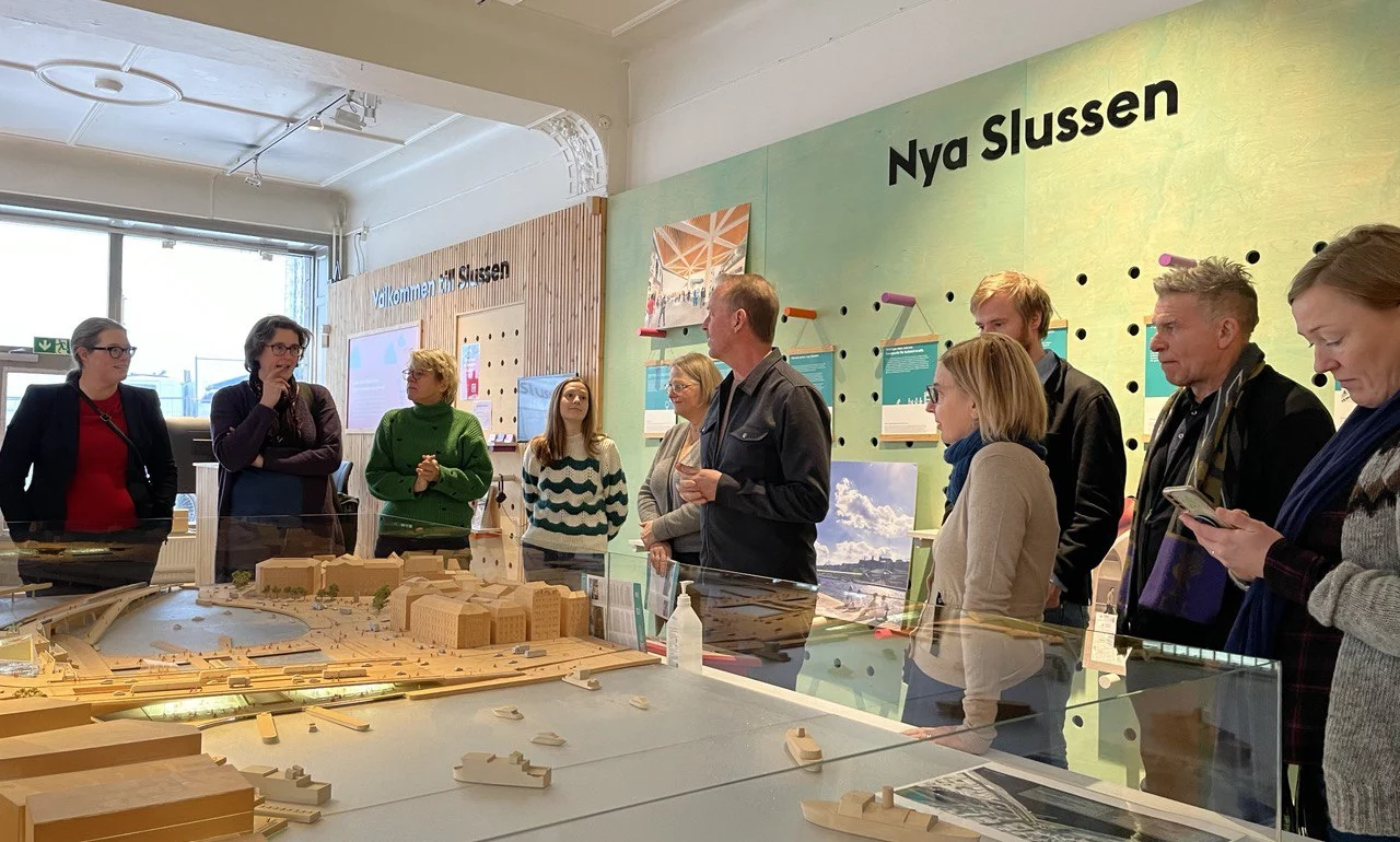 Group of people viewing a model display of the Nya Slussen project at a workshop.