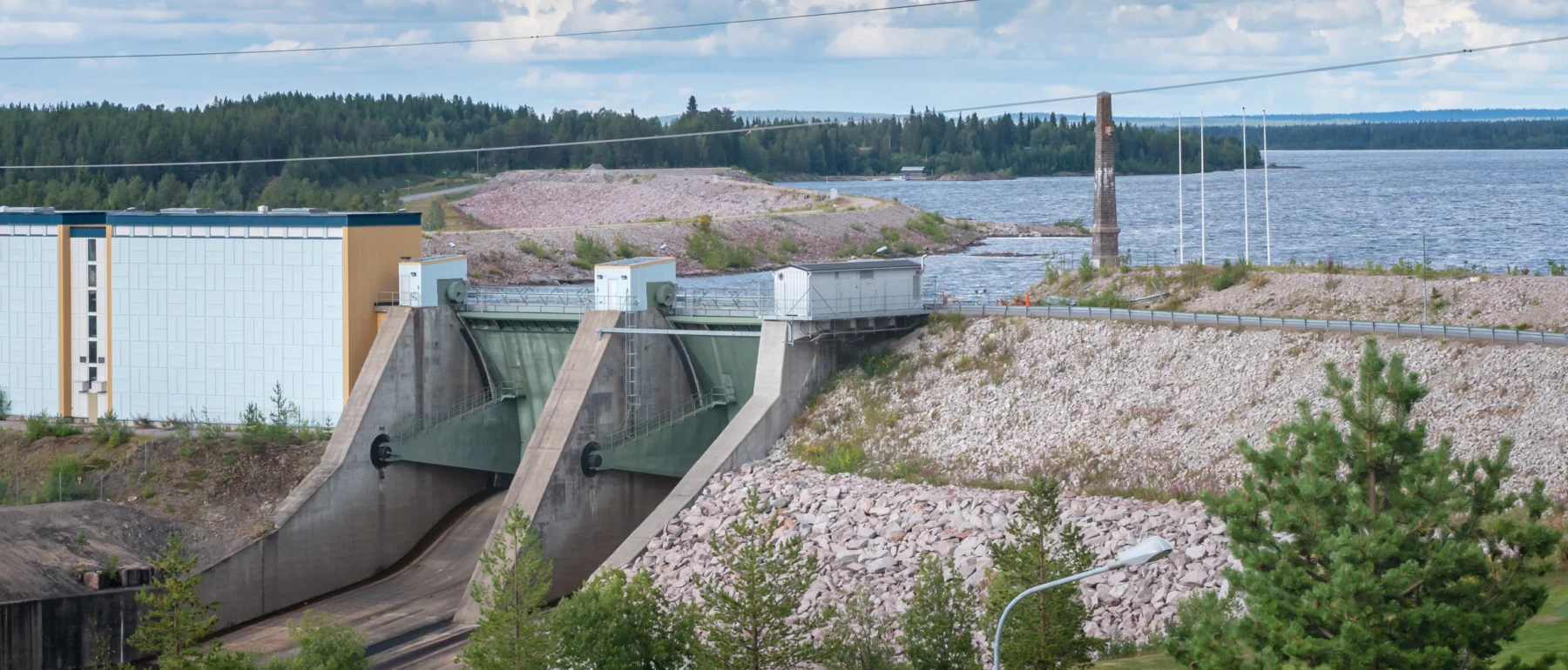 A large dam with water impounded behind it and evergreen trees in the foreground and background.