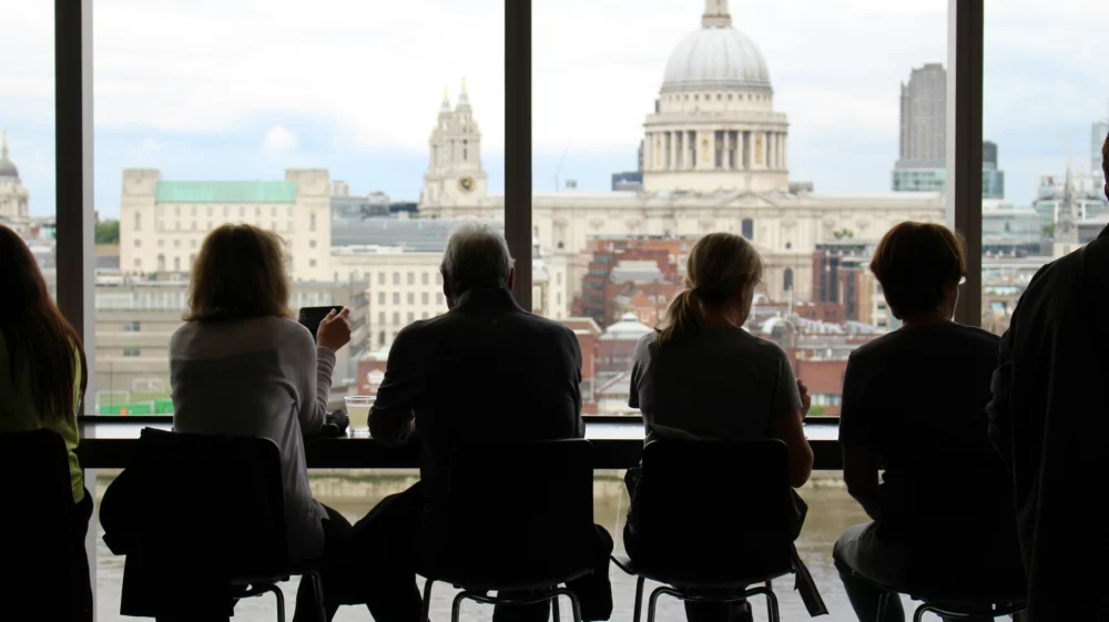 People seated on barstools with the backs to the camera, silhouetted against a London skyline including St Paul's cathedral.